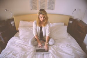 Woman working on her bed using a laptop